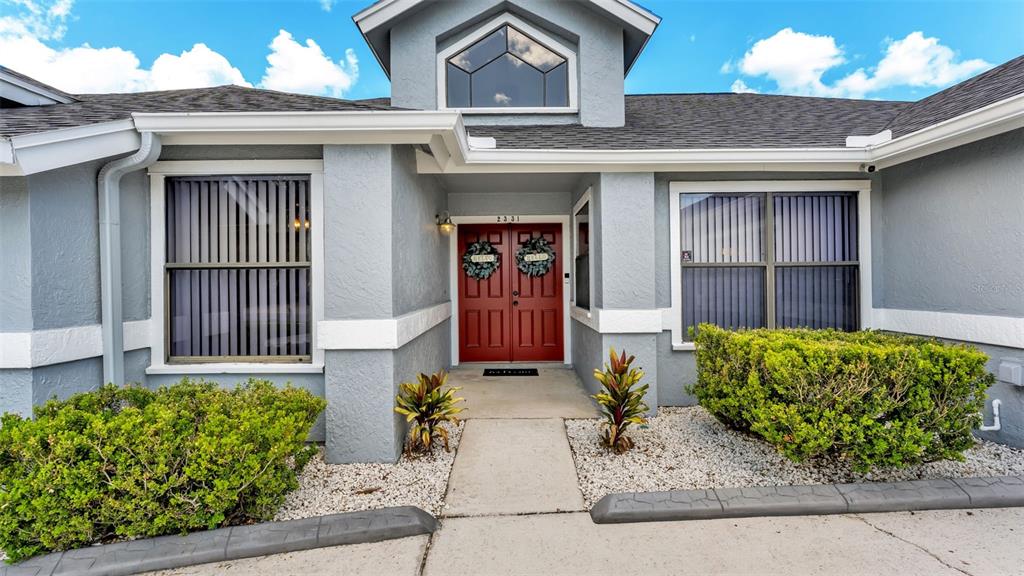 The exterior of a gray house features a red double door and two large windows — 2331 PEPPERCORN STREET, KISSIMMEE, FL