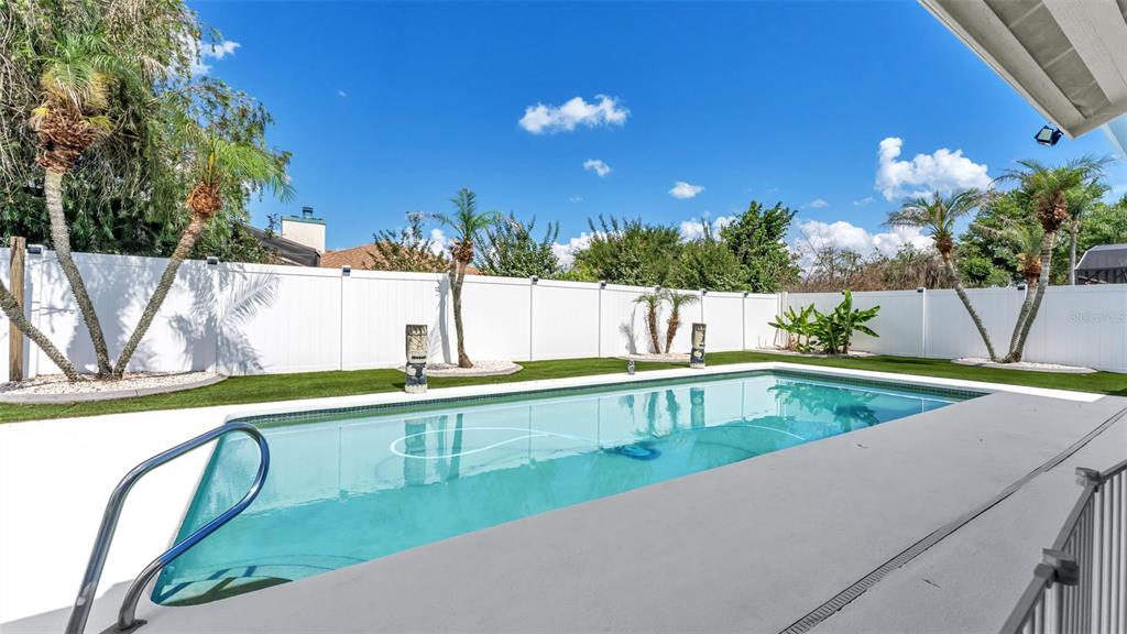 A rectangular swimming pool sits in a backyard with a white fence and palm trees — 2331 PEPPERCORN STREET, KISSIMMEE, FL