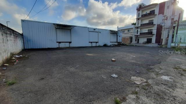 A large, empty gravel lot sits in front of a metal warehouse building — PR 2 INT DELICIAS ST, ARECIBO, PR