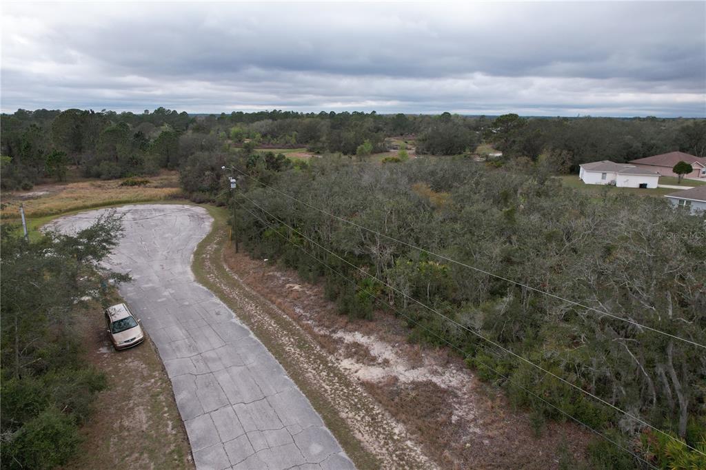 An aerial view shows a paved cul-de-sac next to a wooded lot with power lines — 509 SARASOTA LANE, KISSIMMEE, FL