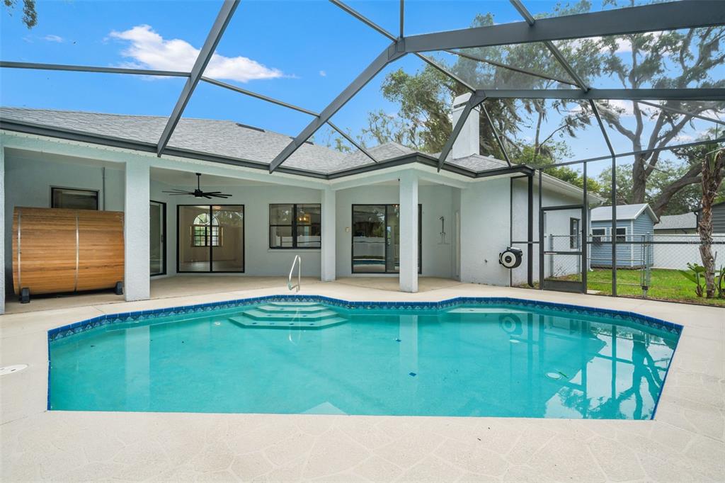 A swimming pool with steps sits inside a screened-in patio next to a house — 9076 GALLUP ROAD, SPRING HILL, FL