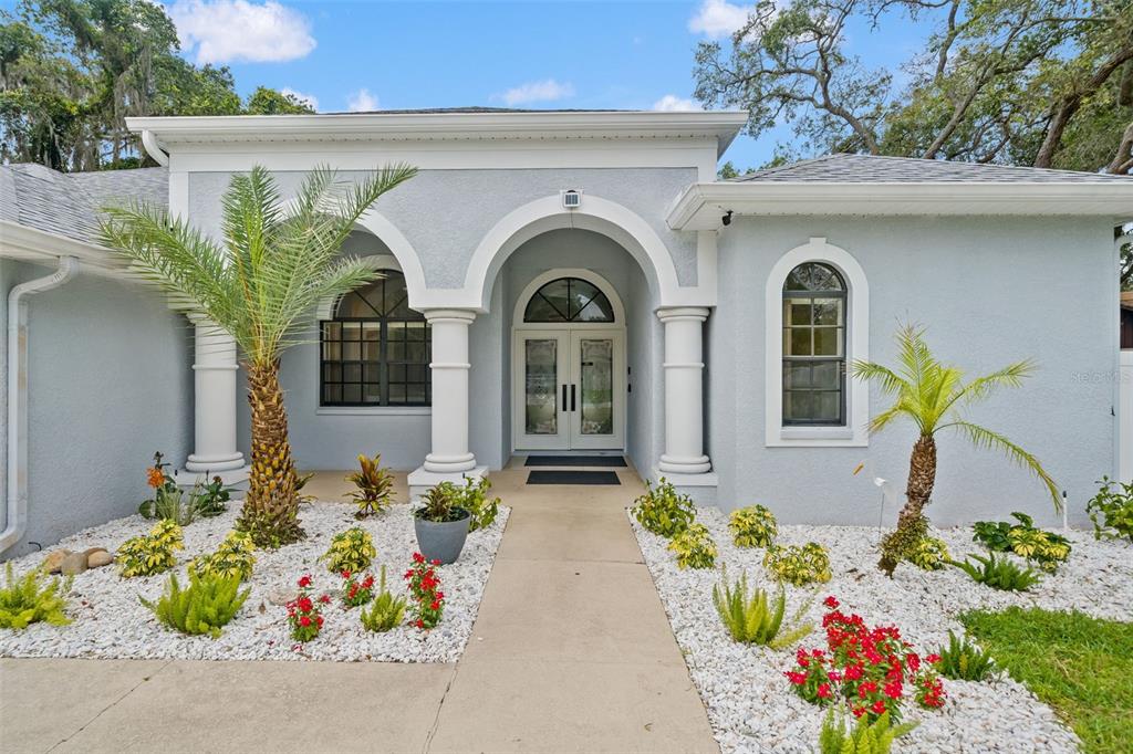 The exterior of a light blue house features a columned entryway and white rock landscaping — 9076 GALLUP ROAD, SPRING HILL, FL