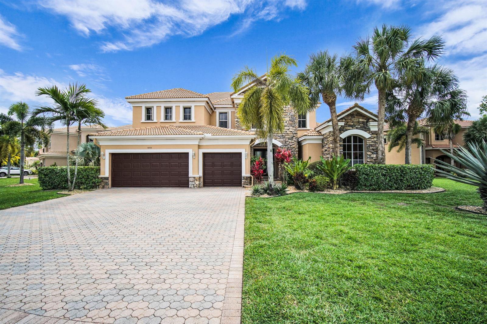 A two-story house with a paved driveway, three-car garage, and palm trees in the front yard — 9192 Pineville Drive, Lake Worth FL 33467, LAKE WORTH, FL