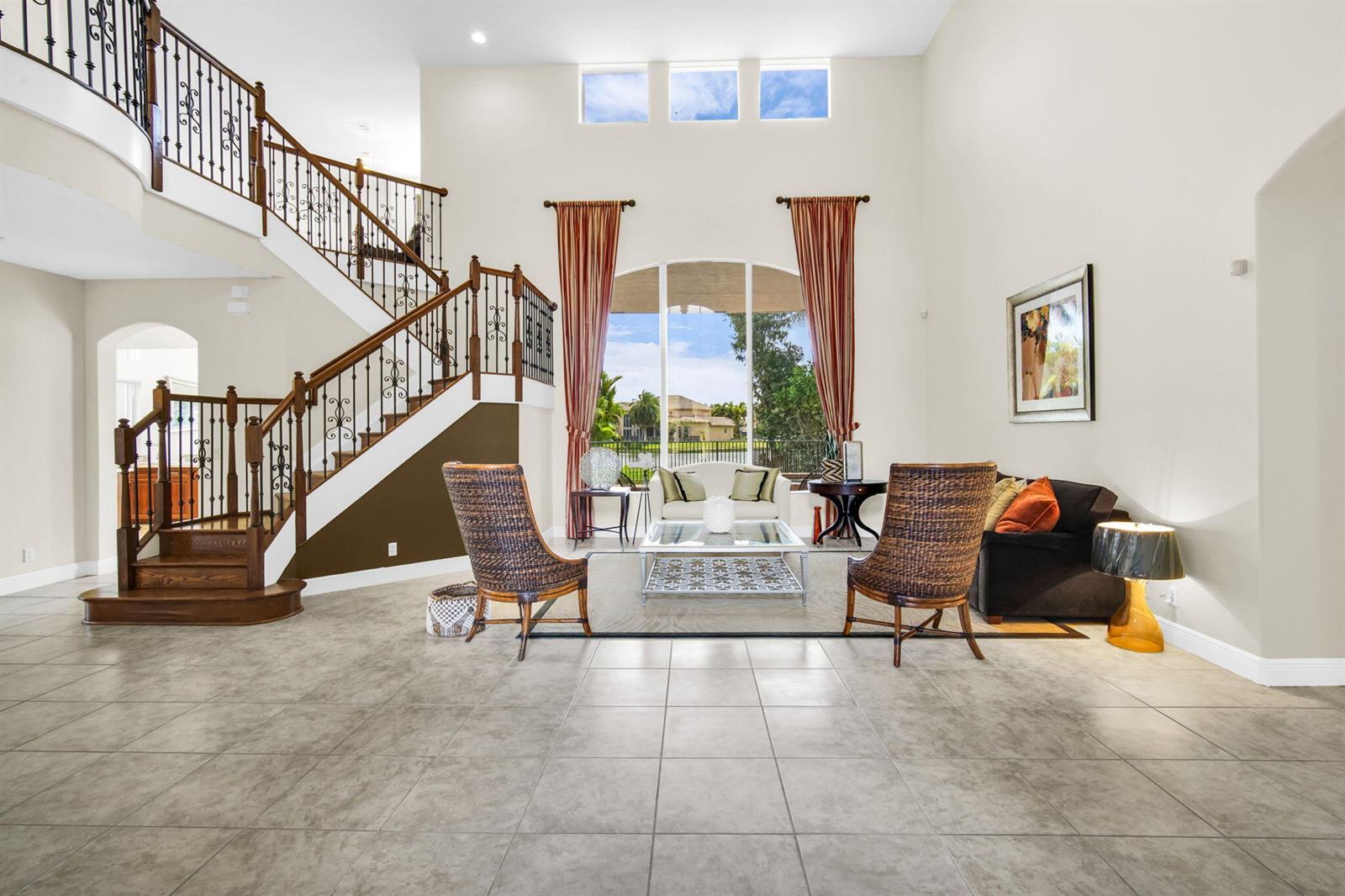 A spacious living room features a grand staircase, tile flooring, and a large arched window — 9192 Pineville Drive, Lake Worth FL 33467, LAKE WORTH, FL