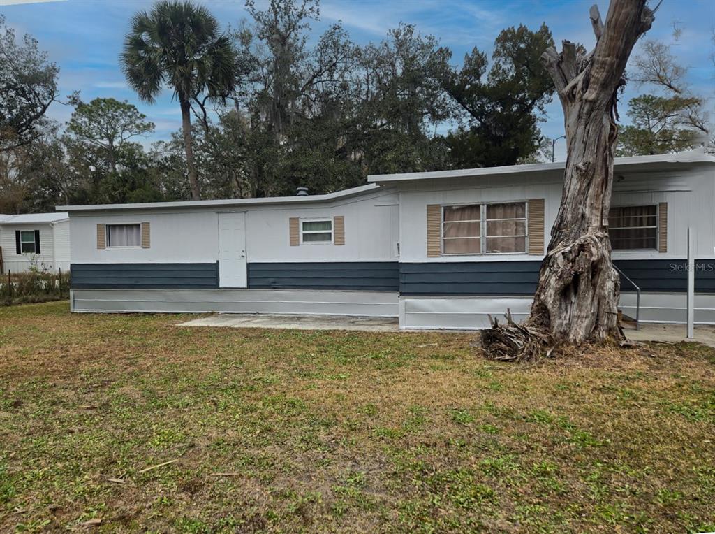 A single-story mobile home with gray and white siding stands beside a large dead tree — 25309 BARTHOLOMEW STREET, CHRISTMAS, FL
