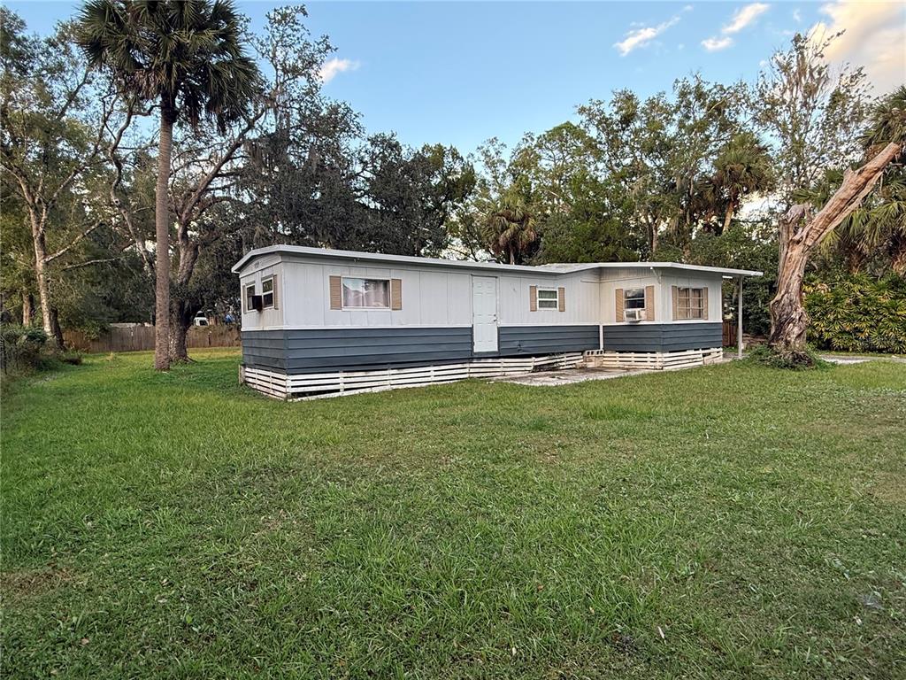 A single-story mobile home with gray and white siding sits on a grassy lot — 25309 BARTHOLOMEW STREET, CHRISTMAS, FL