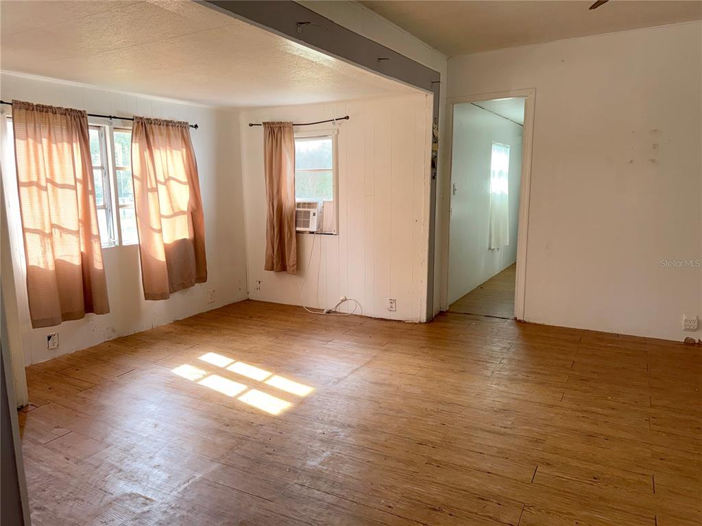 A living room with light wood-look flooring, white walls, and windows with brown curtains — 25309 BARTHOLOMEW STREET, CHRISTMAS, FL