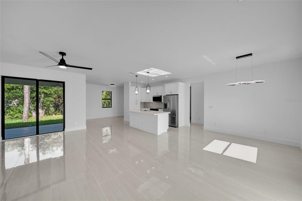 A bright, open-concept kitchen and living area featuring white cabinetry, tile flooring, and sliding doors — 73 FLAMINGO BOULEVARD, PORT CHARLOTTE, FL
