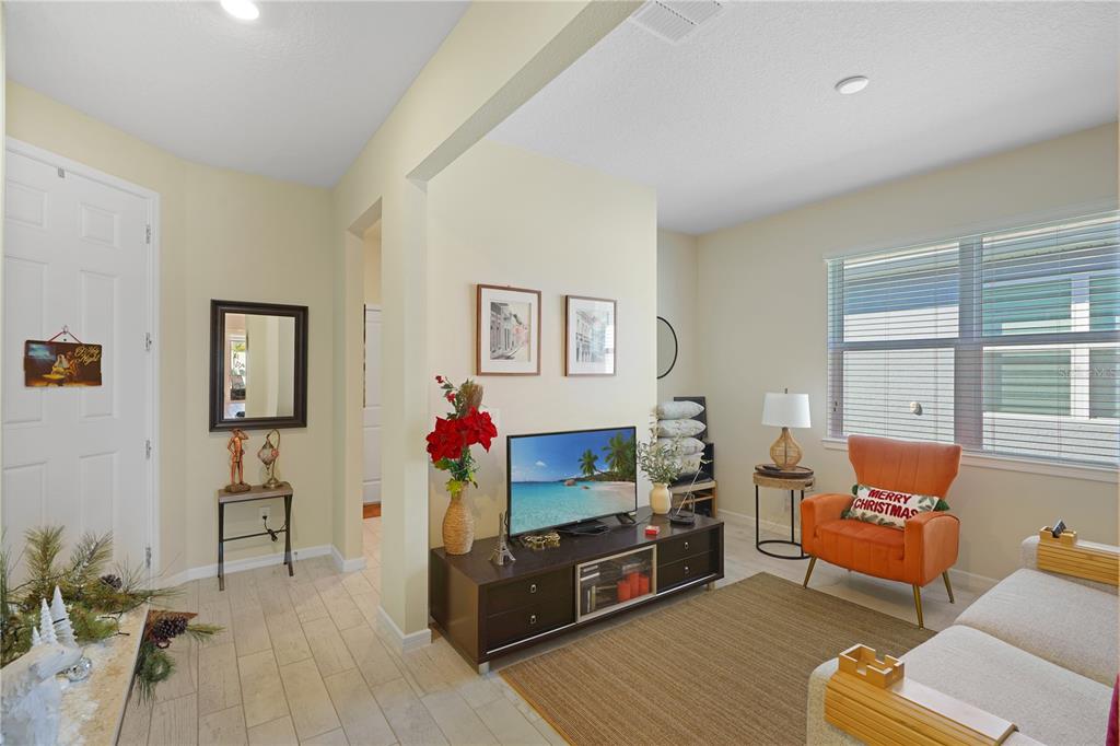 A living room features light tile floors, a television on a dark console, and an orange chair — 1881 SPRING SHOWER CIRCLE, KISSIMMEE, FL
