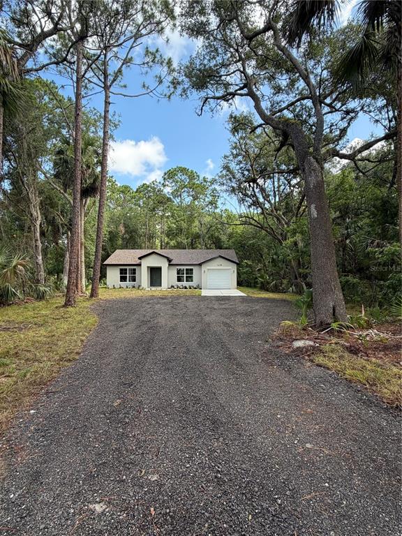 A single-story house with a gravel driveway is surrounded by tall trees — 1438 LAKE HARNEY, GENEVA, FL