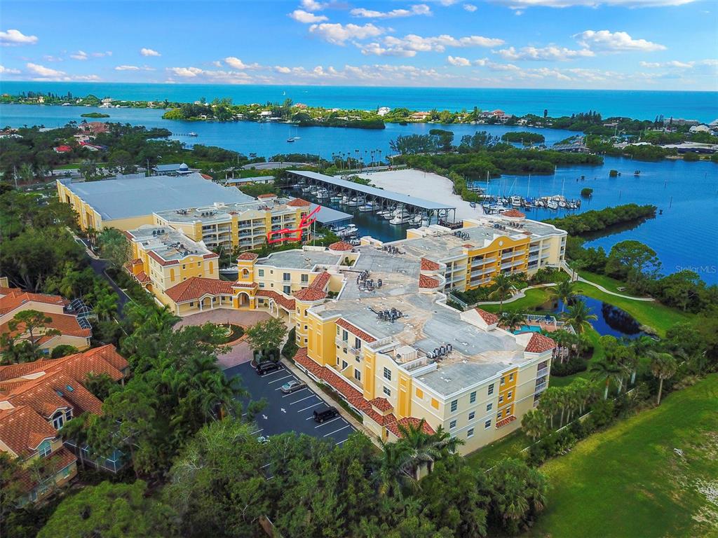 An aerial view shows a large multi-story apartment complex with a marina and bay — 14041 BELLAGIO WAY UNIT 214, OSPREY, FL
