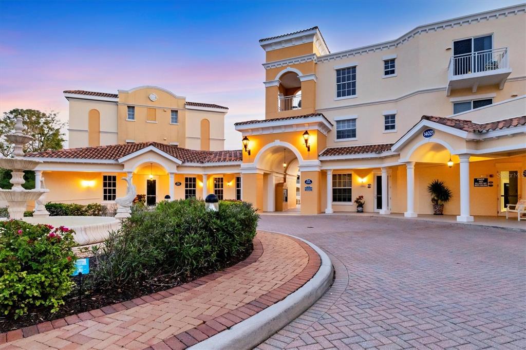 A multi-story stucco building with a brick driveway and a fountain in the foreground — 14041 BELLAGIO WAY UNIT 214, OSPREY, FL