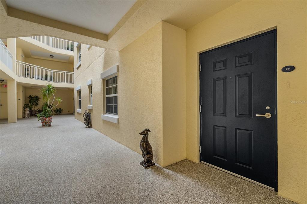 A black front door with the number 214 sits on a yellow stucco exterior hallway — 14041 BELLAGIO WAY UNIT 214, OSPREY, FL