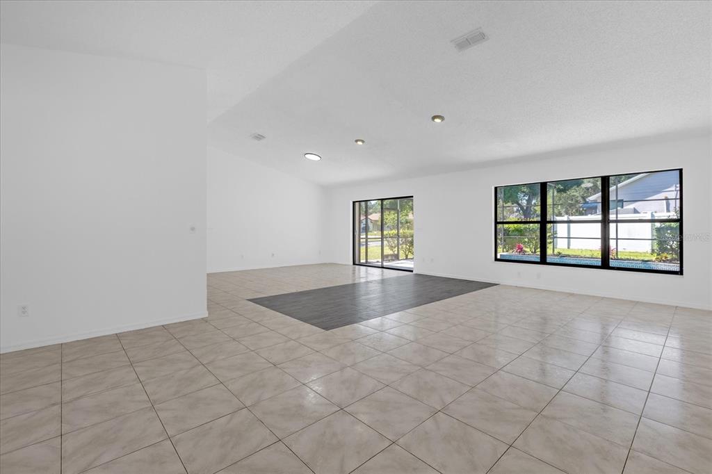 A spacious, empty living area features white walls, light tile flooring, and dark accent flooring — 9011 CHAPMAN OAK COURT, WINDERMERE, FL