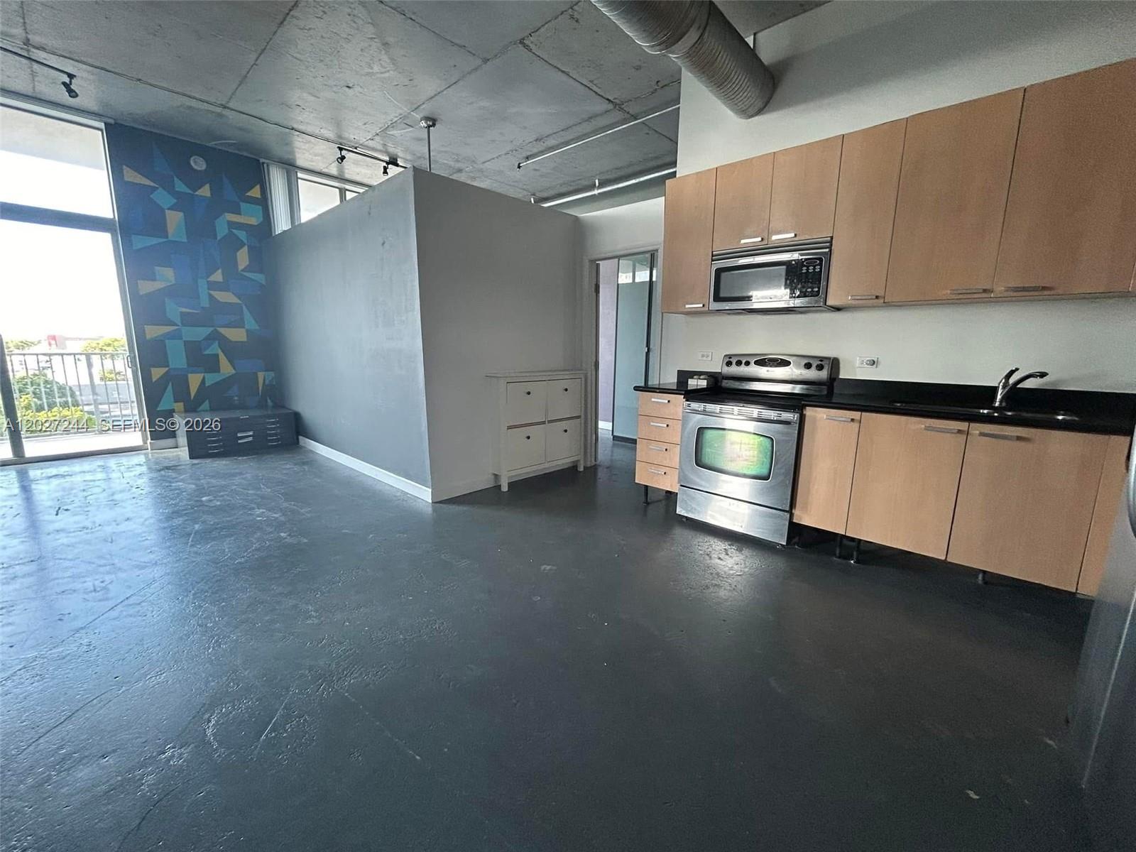 A kitchen with light wood cabinets and stainless steel appliances sits in an industrial loft — 2100 Van Buren St # 506, Hollywood FL 33020, HOLLYWOOD, FL