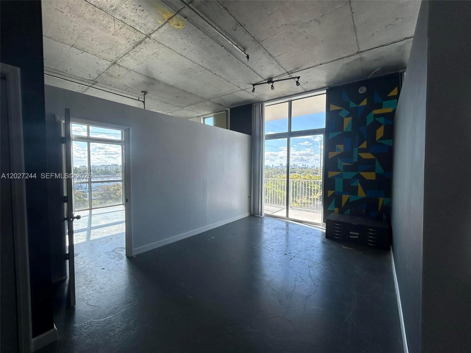 An interior room features a concrete ceiling, dark flooring, and a large geometric accent wall — 2100 Van Buren St # 506, Hollywood FL 33020, HOLLYWOOD, FL
