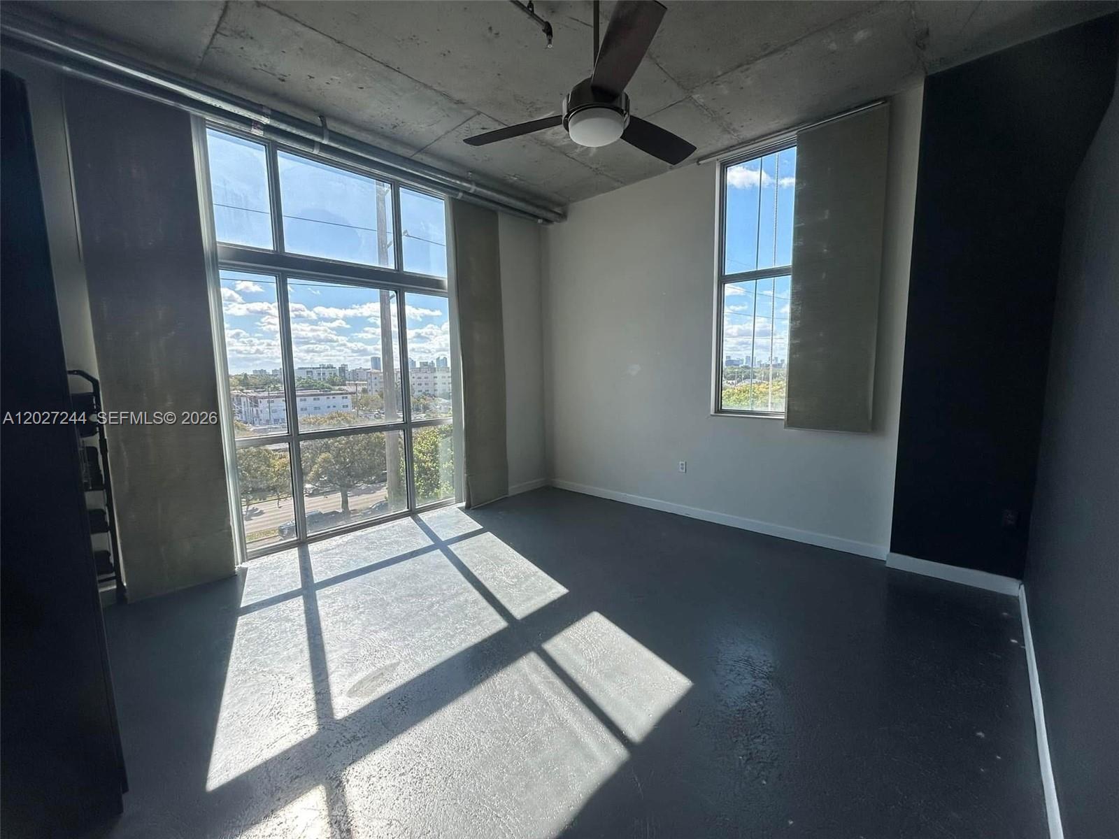 An empty room features concrete ceilings, gray floors, large windows, and a ceiling fan — 2100 Van Buren St # 506, Hollywood FL 33020, HOLLYWOOD, FL