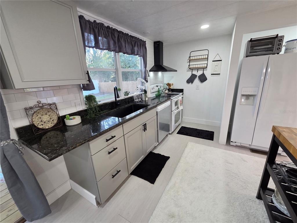 A kitchen features gray cabinets, dark granite countertops, a white subway tile backsplash, and appliances — 1846 FRUITLAND PARK BOULEVARD, FRUITLAND PARK, FL