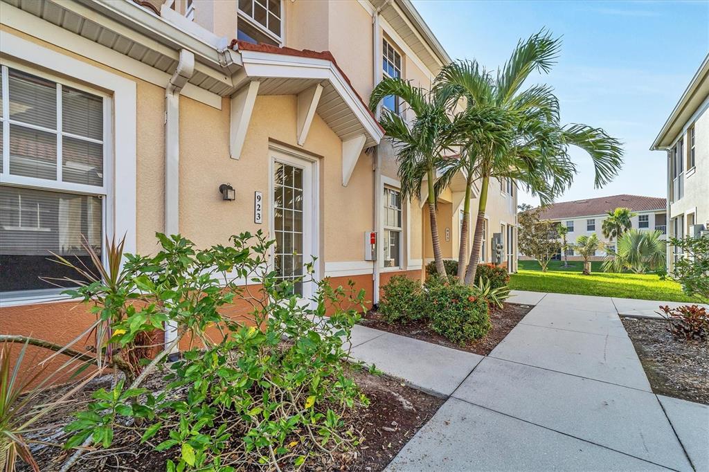 The exterior of a multi-story residential building features a tan facade, a white-framed door, and landscaping — 240 W END DRIVE UNIT 923, PUNTA GORDA, FL