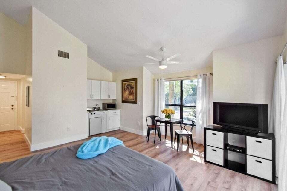 A studio apartment featuring a kitchenette, dining area, bed, and television stand on wood flooring — 11863 Wimbledon Circle # 508, Wellington FL 33414, WELLINGTON, FL