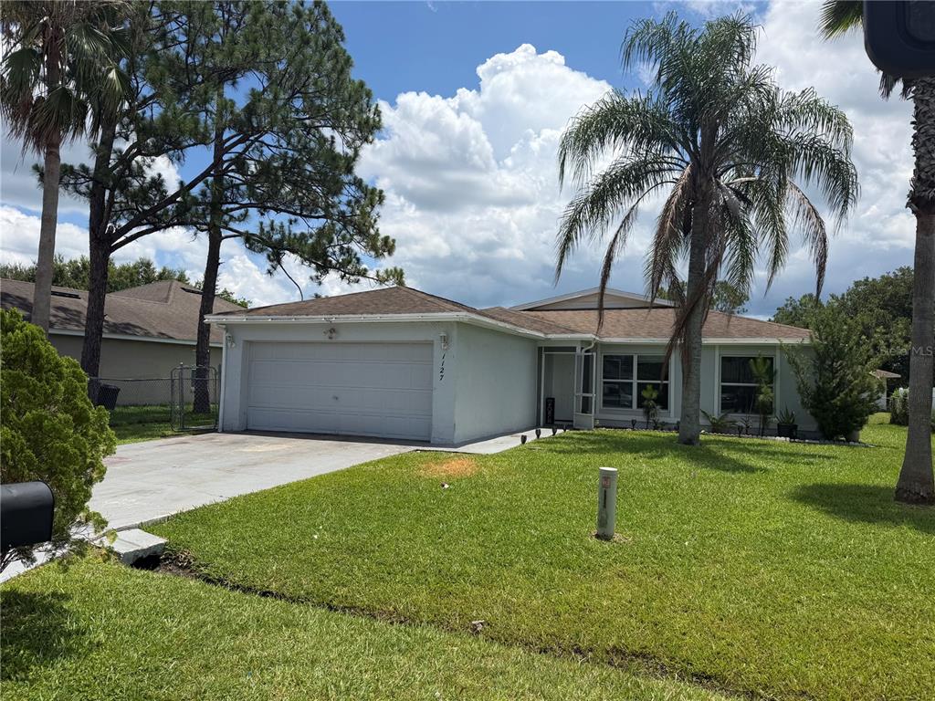 A single-story house with a white exterior, a two-car garage, and a palm tree — 1127 GARDANNE COURT, KISSIMMEE, FL