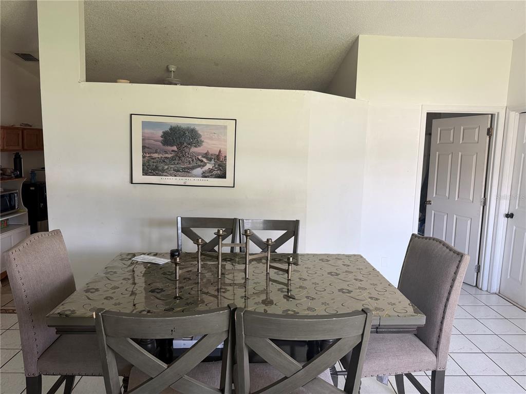 A dining room features a glass-topped table with gray chairs and a framed wall print — 1127 GARDANNE COURT, KISSIMMEE, FL