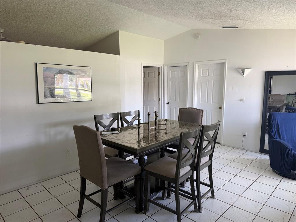 A dining area features a dark table with six chairs on a white tiled floor — 1127 GARDANNE COURT, KISSIMMEE, FL