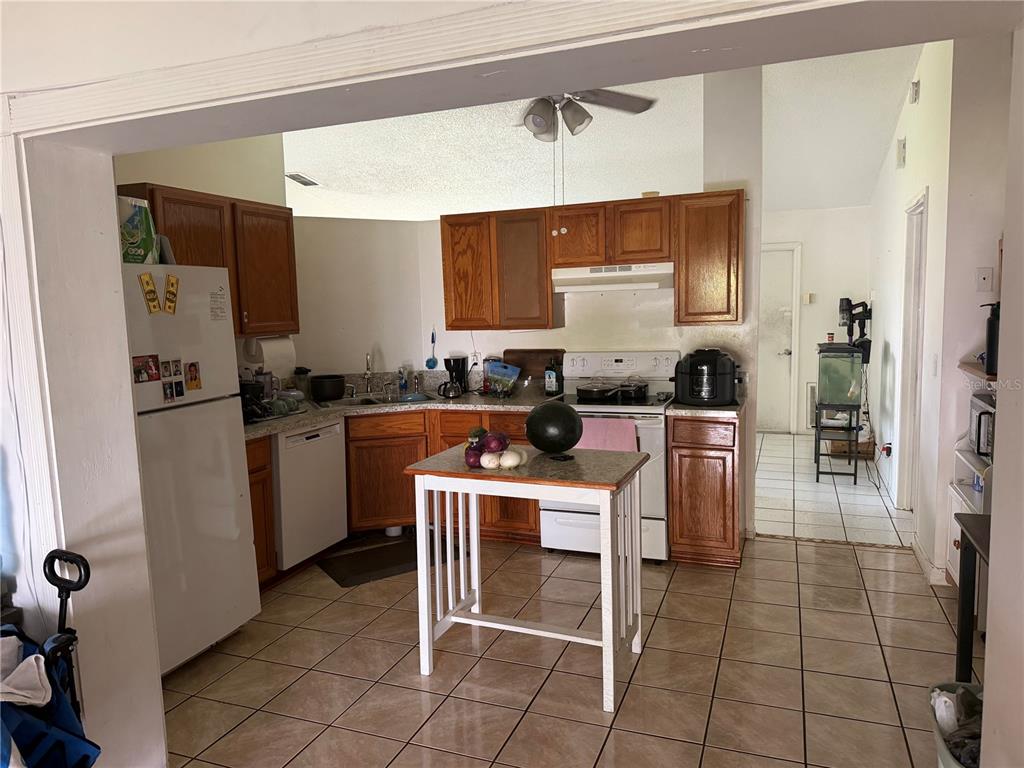 A kitchen features wood cabinets, tile flooring, a center island, and white appliances — 1127 GARDANNE COURT, KISSIMMEE, FL