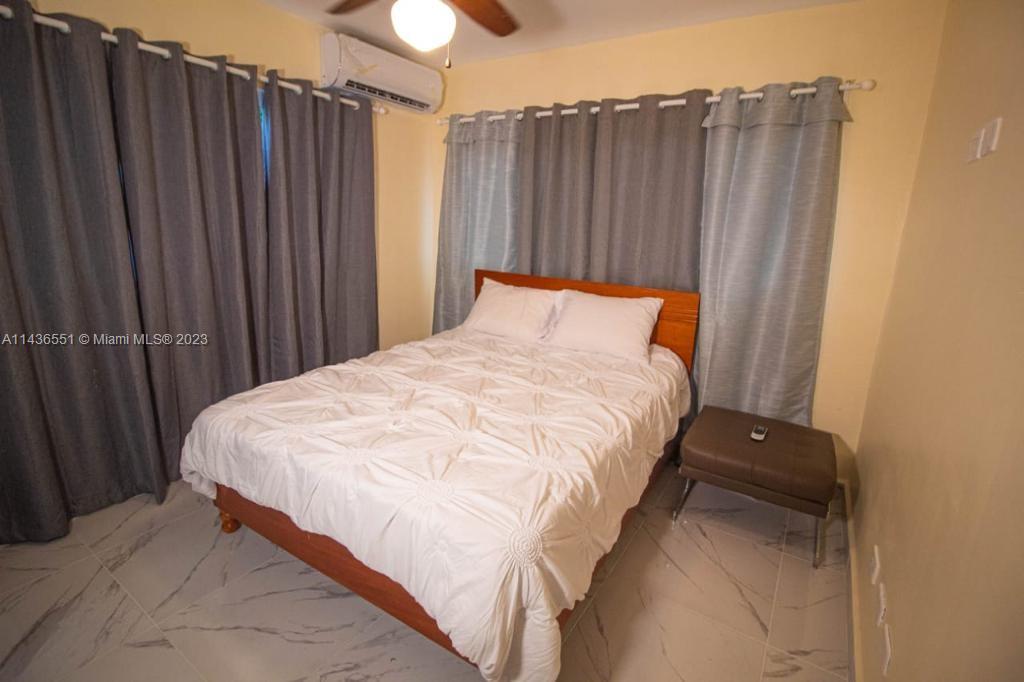 A bedroom features a bed with a white comforter, gray curtains, and tiled flooring — 1234 Carretera Sanchez # 1G, DR, DR