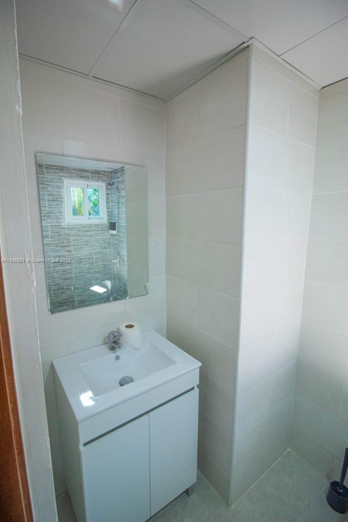 A bathroom features a white vanity, a square mirror, and light-colored tiled walls — 1234 Carretera Sanchez # 1G, DR, DR