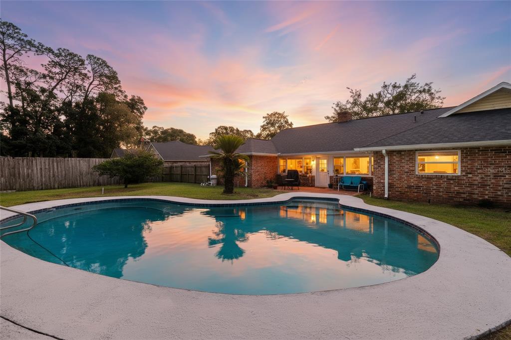 A backyard with a swimming pool, a brick house, and a wooden fence at sunset — 4517 SE 2ND PLACE, OCALA, FL
