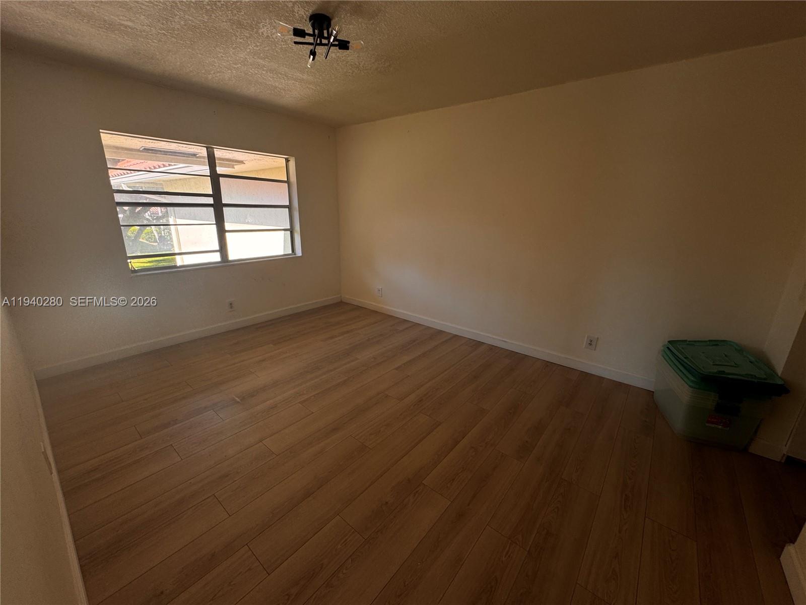 An empty room features light wood-look flooring, plain walls, and a single window — 1100 NW 13th St # 294D, Boca Raton FL 33486, BOCA RATON, FL