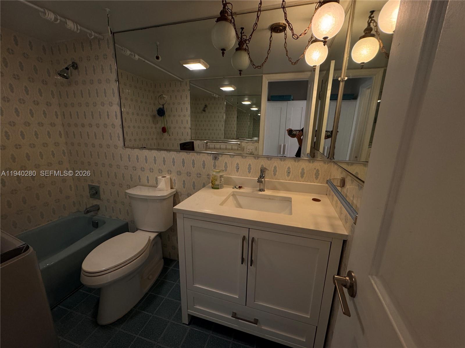 A bathroom features a blue bathtub, a white vanity, a toilet, and patterned wallpaper — 1100 NW 13th St # 294D, Boca Raton FL 33486, BOCA RATON, FL