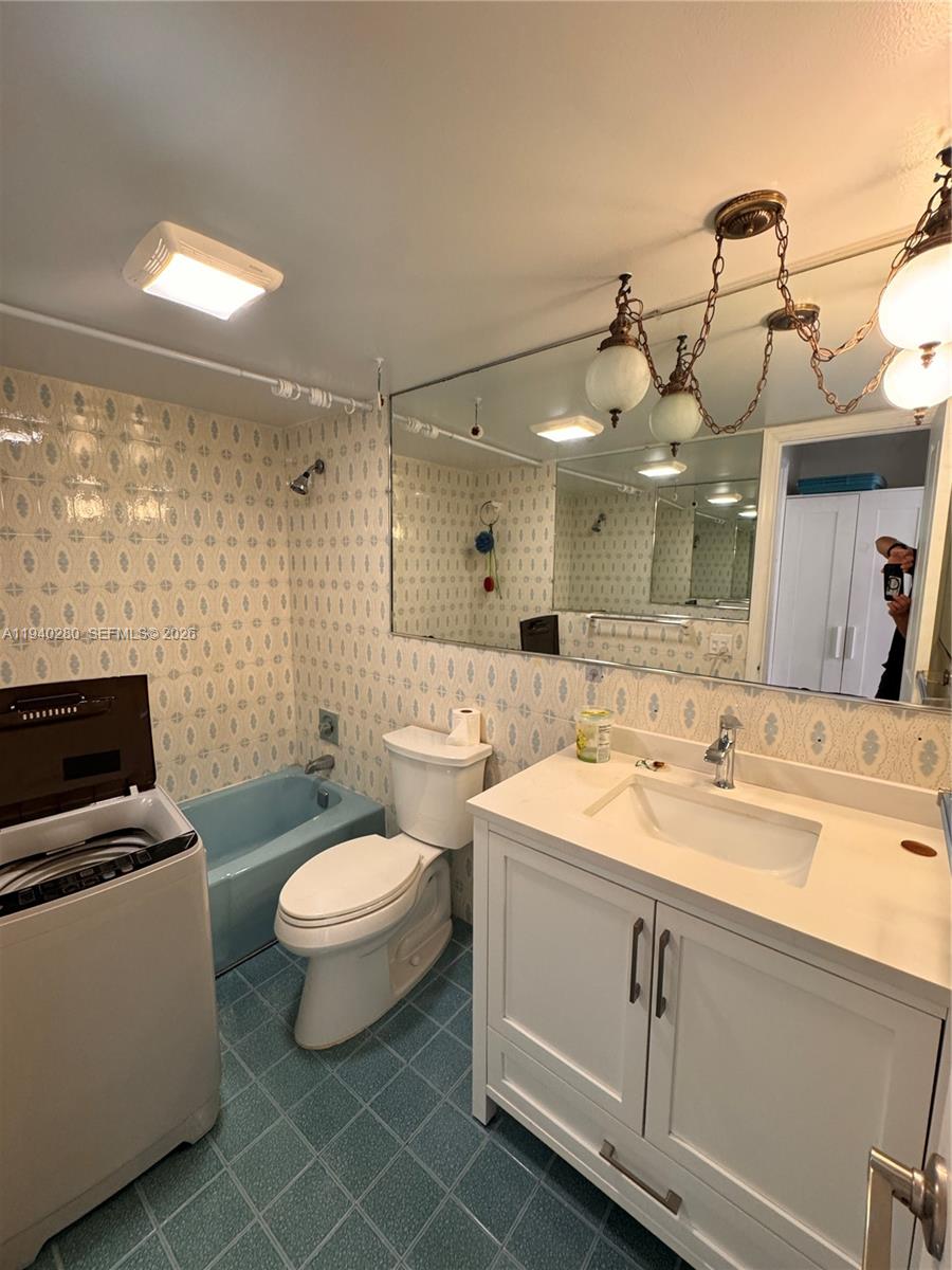 A bathroom features a blue bathtub, a white vanity, a toilet, and patterned wallpaper — 1100 NW 13th St # 294D, Boca Raton FL 33486, BOCA RATON, FL
