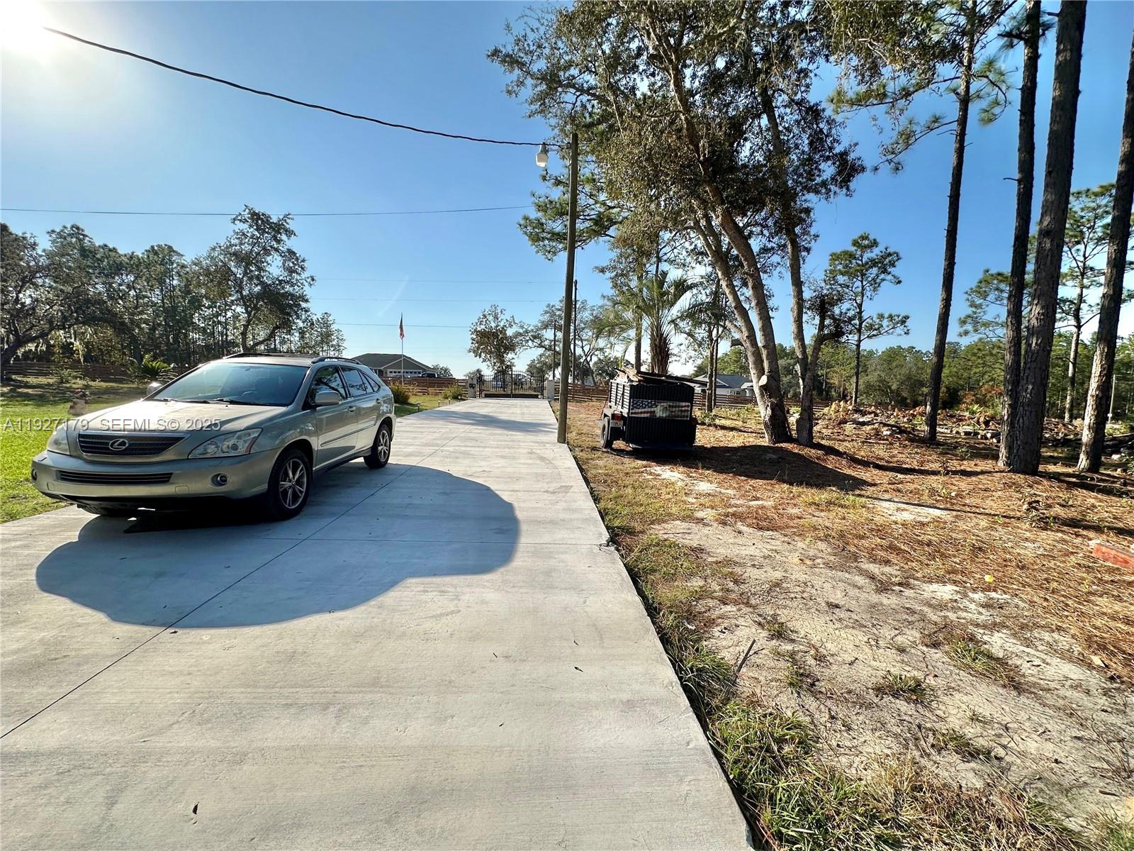 A silver SUV is parked on a concrete driveway next to a trailer and trees — 6525 SW 138th ter, Ocala FL 33481, OCALA, FL