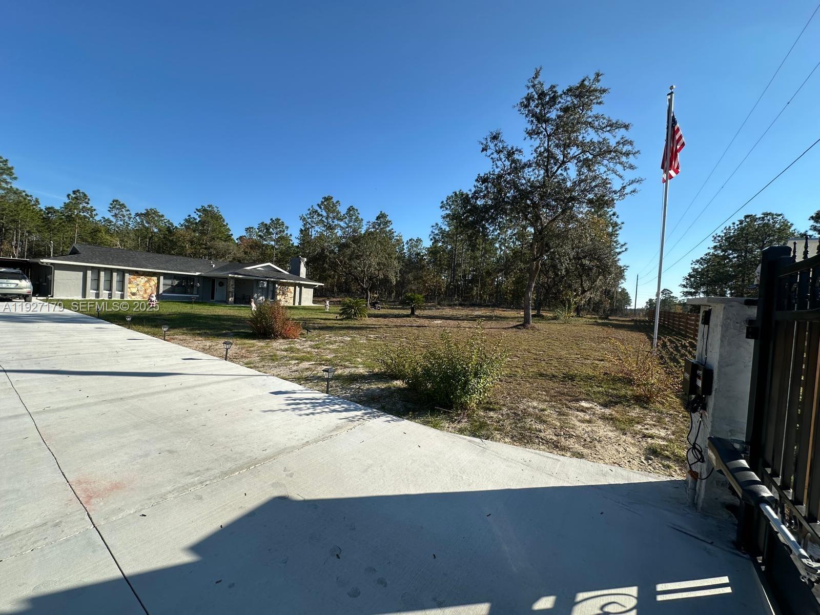 A concrete driveway leads toward a single-story house with a stone facade and American flag — 6525 SW 138th ter, Ocala FL 33481, OCALA, FL