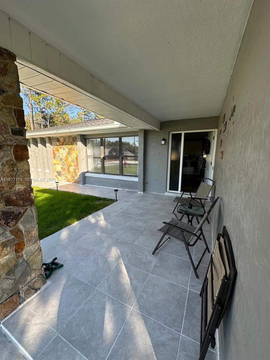 A covered patio features gray tiled flooring, stone accents, and outdoor chairs near the entrance — 6525 SW 138th ter, Ocala FL 33481, OCALA, FL