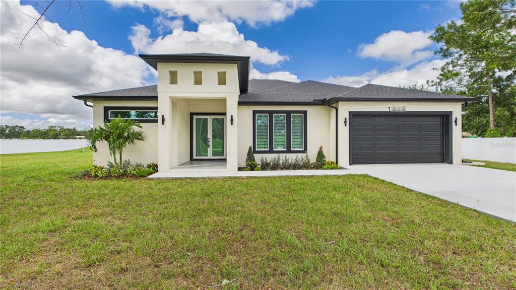 A modern, single-story house with a cream stucco exterior, black trim, and a two-car garage — 1515 30TH STREET SE, RUSKIN, FL