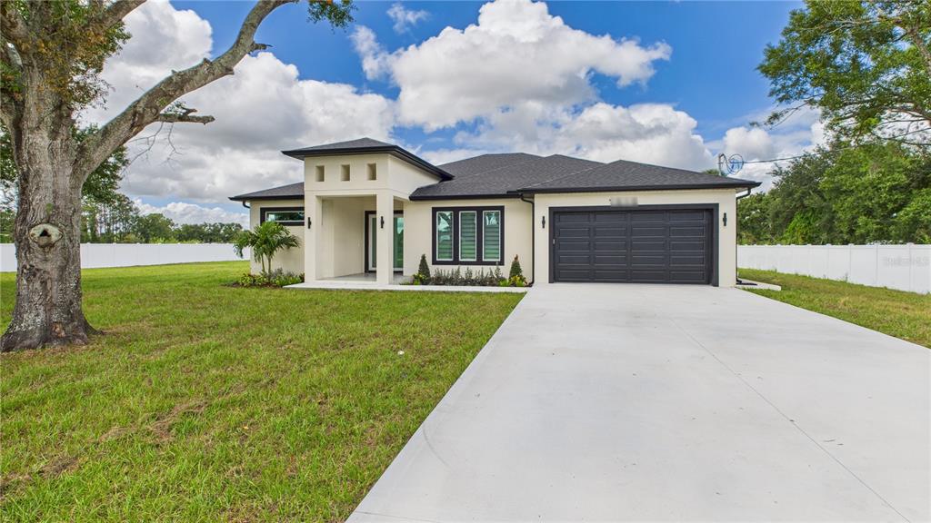 A modern, single-story house with a black garage door and a concrete driveway — 1515 30TH STREET SE, RUSKIN, FL