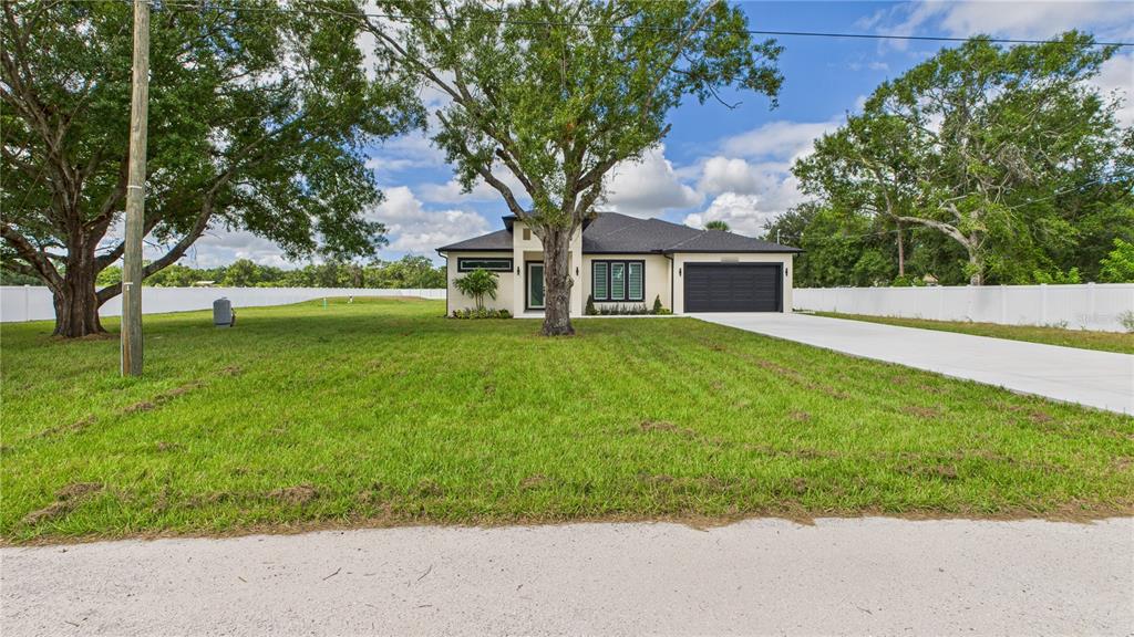 A single-story house with a black garage door and white exterior sits on a grassy lot — 1515 30TH STREET SE, RUSKIN, FL