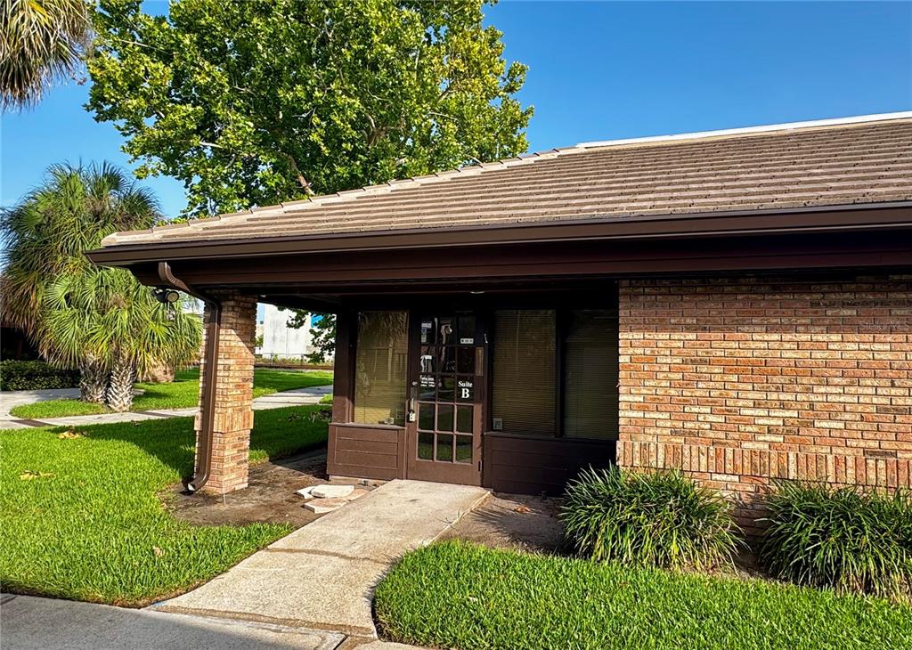 A brick office building exterior features a glass-paned door labeled Suite B and landscaping — 200 E MONUMENT AVENUE UNIT B, KISSIMMEE, FL