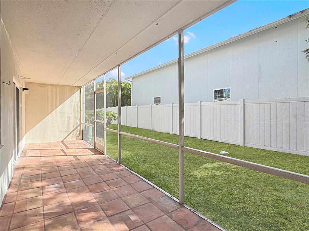 A screened-in patio with tiled flooring overlooks a grassy backyard enclosed by a white fence — 4435 1ST STREET NE UNIT 103, ST PETERSBURG, FL