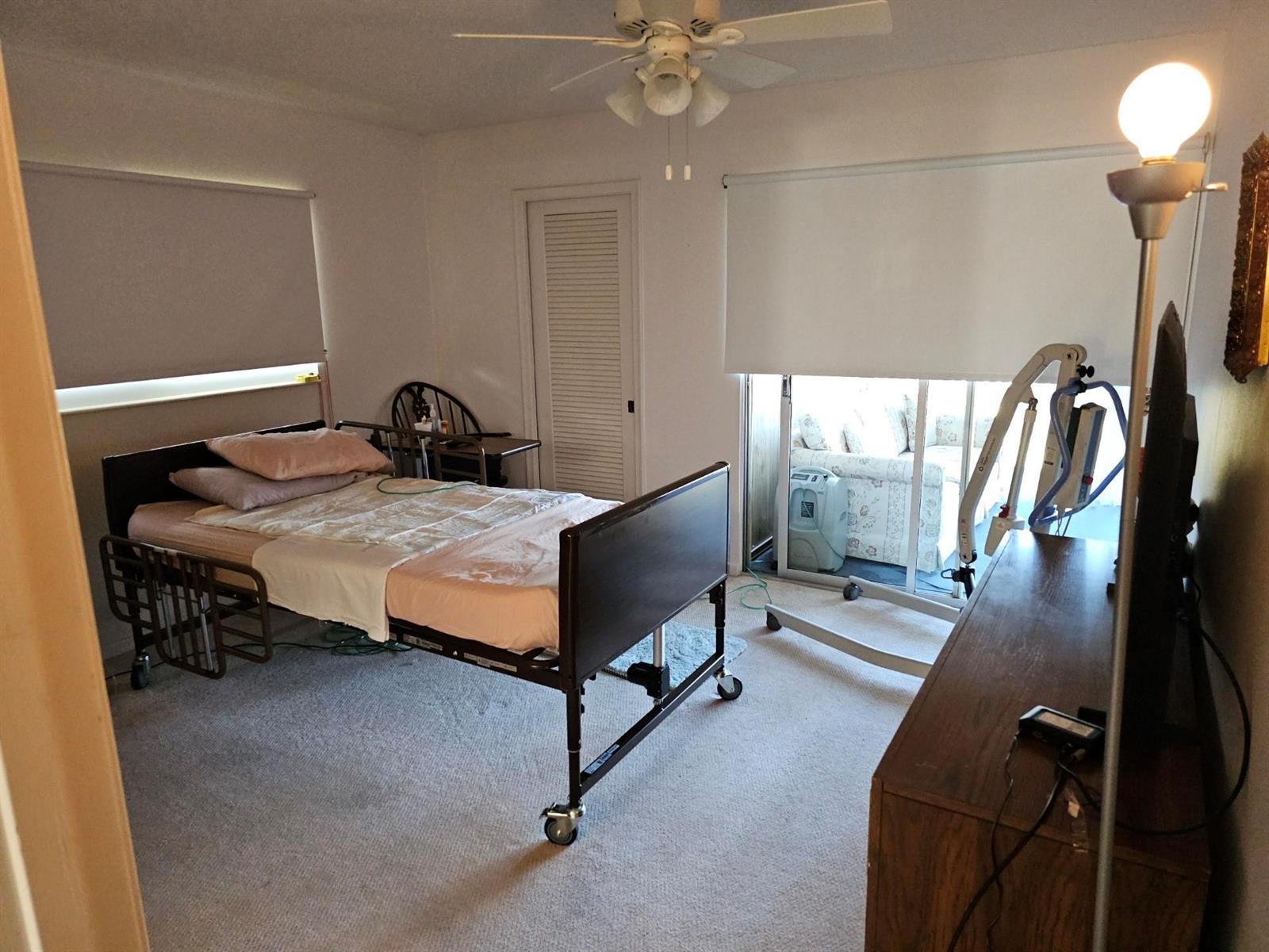 A bedroom with a hospital bed, patient lift, and sliding glass doors leading to a patio — 4015 Lyndhurst I # 4015, Deerfield Beach FL 33442, DEERFIELD BEACH, FL