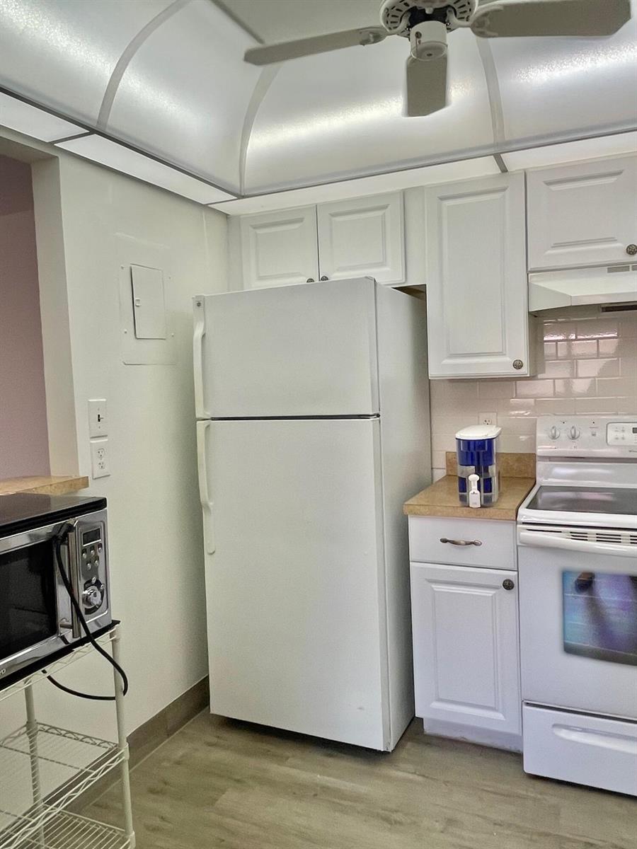 A kitchen features white cabinets, a white refrigerator, a white stove, and a ceiling fan — 654 Saxony N, Delray Beach FL 33446, DELRAY BEACH, FL