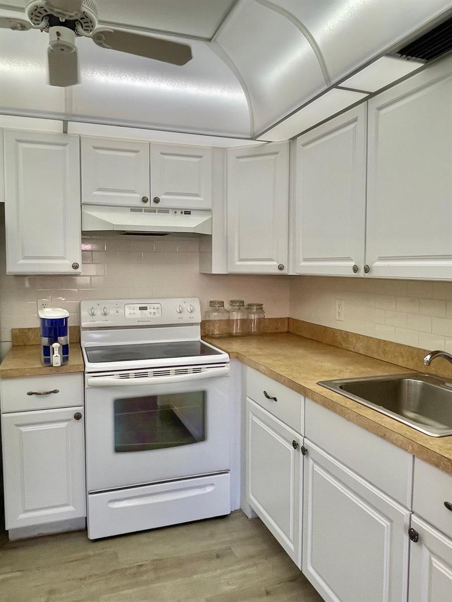 A kitchen features white cabinets, tan laminate countertops, a white electric stove, and subway tile — 654 Saxony N, Delray Beach FL 33446, DELRAY BEACH, FL