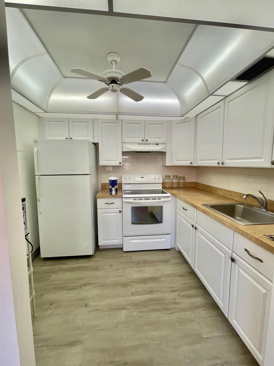 A kitchen features white cabinetry, a white refrigerator, a white stove, and tan countertops — 654 Saxony N, Delray Beach FL 33446, DELRAY BEACH, FL