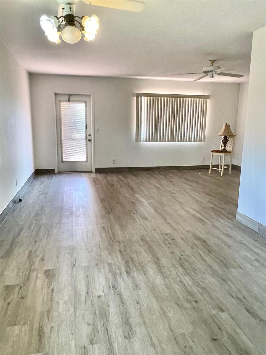 An empty room features light wood-look flooring, white walls, a ceiling fan, and a glass door — 654 Saxony N, Delray Beach FL 33446, DELRAY BEACH, FL