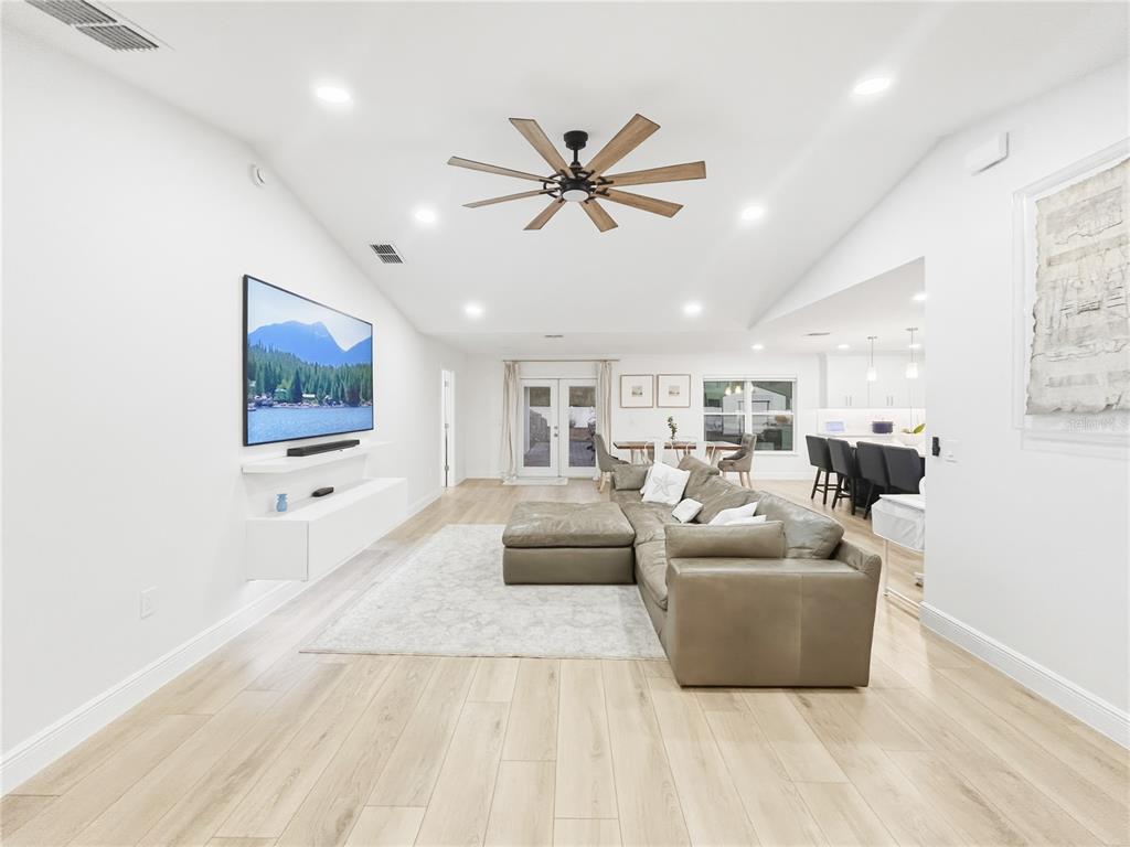 A bright, open-concept living room features light wood flooring, a sectional sofa, and a wall-mounted television — 2285 FOX WOOD COURT, ST CLOUD, FL