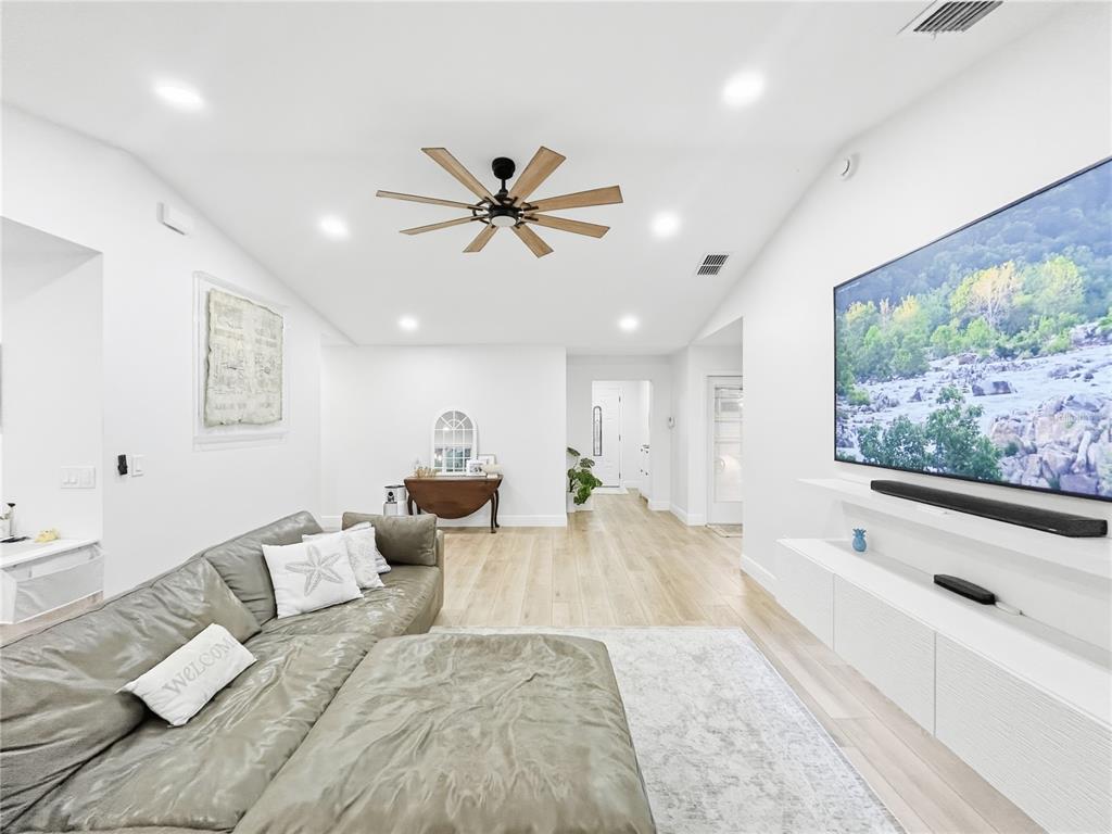 A bright living room features a large gray sectional, a wall-mounted television, and wood flooring — 2285 FOX WOOD COURT, ST CLOUD, FL