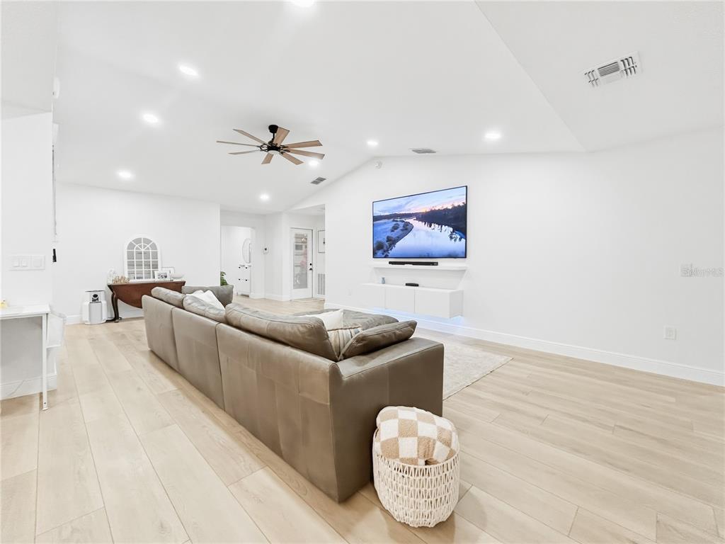 A spacious living room features light wood flooring, a large sectional sofa, and a wall-mounted television — 2285 FOX WOOD COURT, ST CLOUD, FL